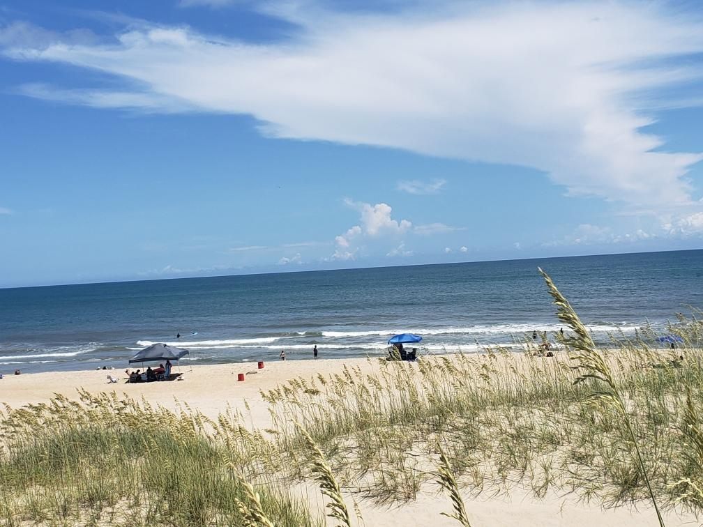 A summer beach day on the sand in Avon, umbrellas and sea oats in the dunes